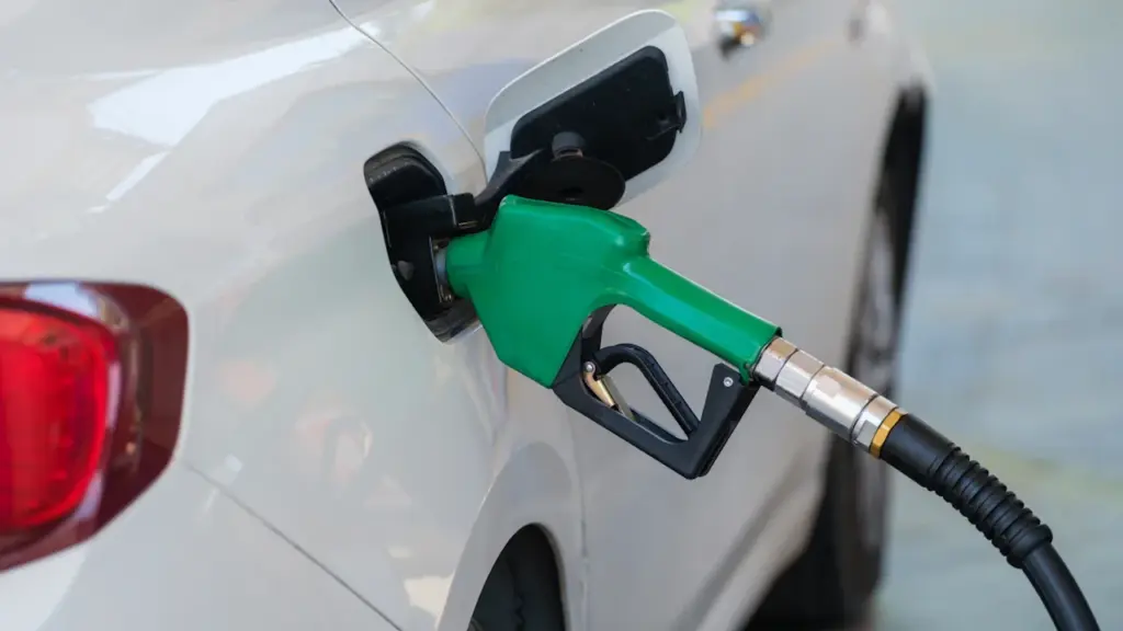 Eine grüne Zapfpistole beim Betanken eines weißen Pkw an der Tankstelle.