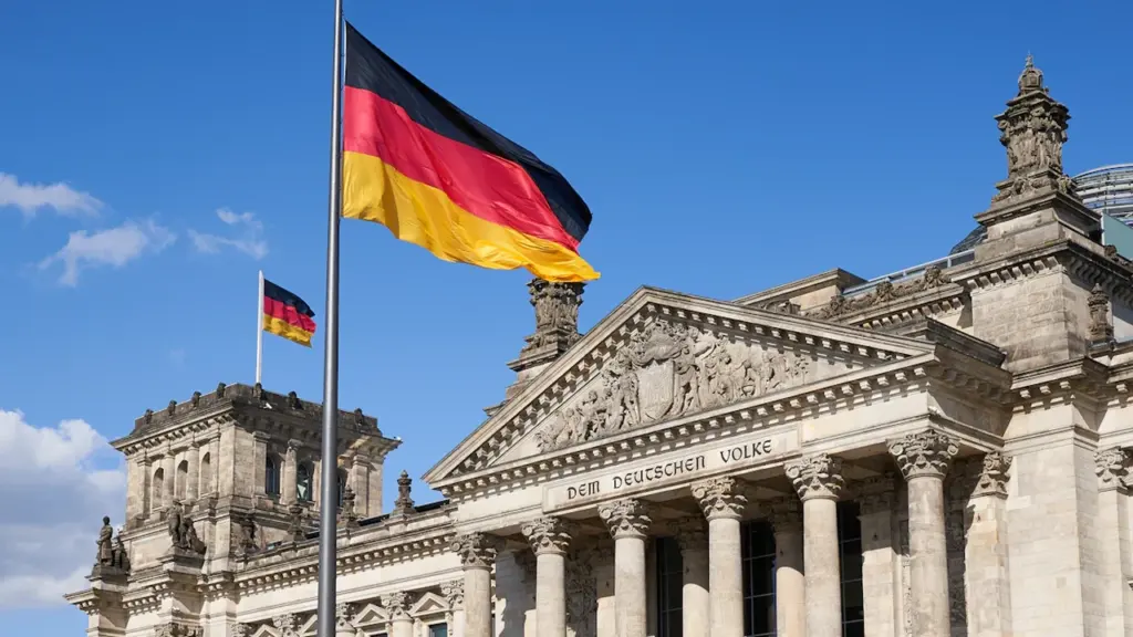 Deutscher Reichstag in Berlin mit wehender deutscher Flagge bei Tageslicht.