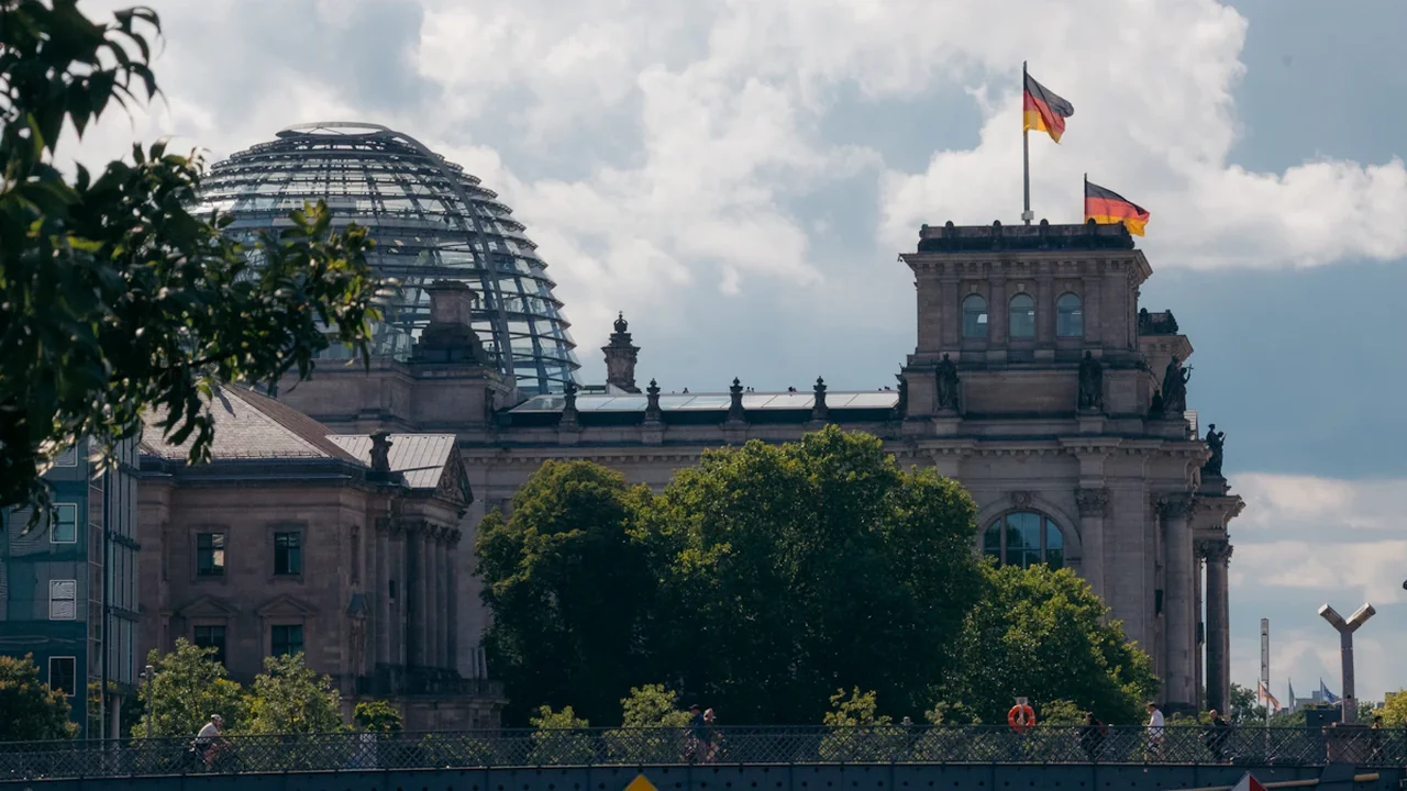 Das Reichstagsgebäude in Berlin unter blauem Himmel mit wehenden deutschen Flaggen im Vordergrund.