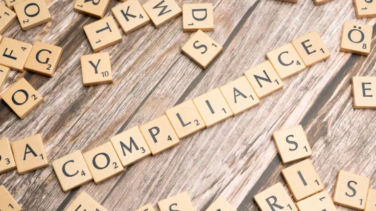 Holzbuchstaben bilden das Wort Compliance auf einem hölzernen Schreibtischhintergrund.