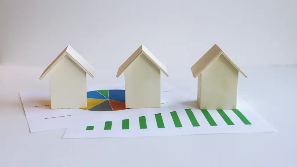Drei kleine Holzhäuser auf einem Finanzdiagramm mit grüner Balkengrafik und Tortendiagramm.
