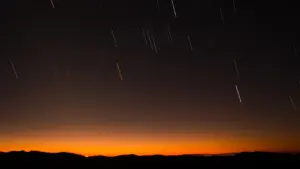 Lange Belichtungsaufnahme eines Sternenhimmels mit sichtbaren Lichtspuren über einer dunklen Hügellandschaft in Deutschland.