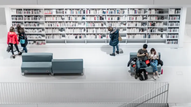 Besucher in einer modernen Bibliothek vor einem gut gefüllten Bücherregal in Deutschland.