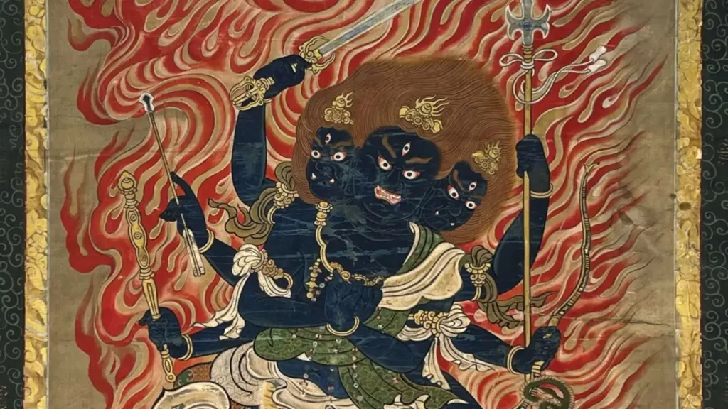Ein blauhäutiges, dreiköpfiges buddhistisches Wesen mit sechs Armen vor einem leuchtend roten Flammenhintergrund.