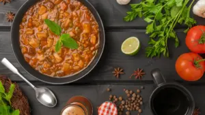 Dunkle Schüssel mit Linseneintopf, serviert auf einem rustikalen Holztisch mit frischen Zutaten.