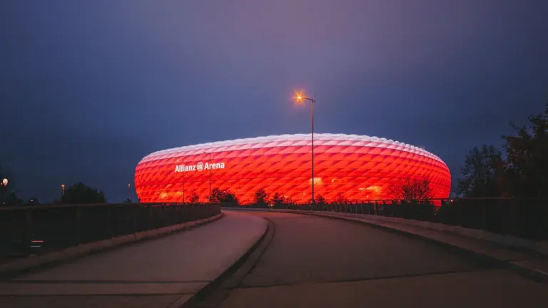 Die beleuchtete Allianz Arena in München bei Nacht aus einer Panorama-Perspektive.