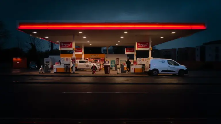 Eine beleuchtete Tankstelle bei Nacht mit einem weißen Auto an der Zapfsäule.