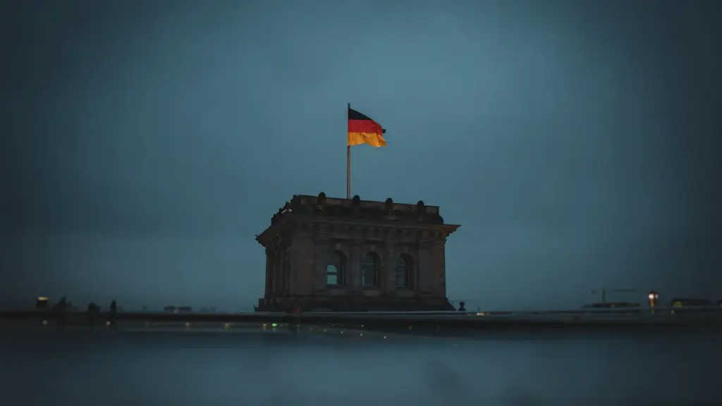 Die deutsche Flagge weht über dem beleuchteten Reichstagsgebäude bei düsterer, dunkler Abenddämmerung in Berlin.