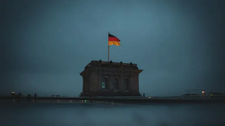 Die deutsche Flagge weht über dem beleuchteten Reichstagsgebäude bei düsterer, dunkler Abenddämmerung in Berlin.