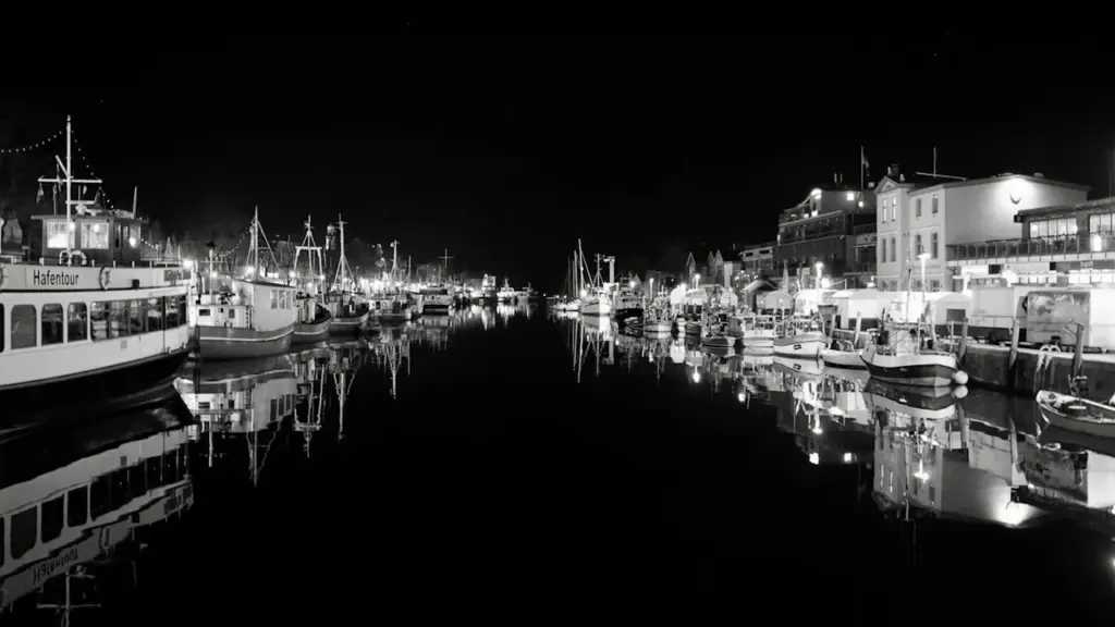 Nächtlicher Blick auf die Hafenbecken und festgemachte Schiffe in Warnemünde bei Dunkelheit.