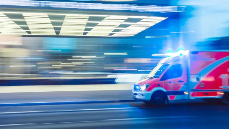 Ein Rettungswagen fährt nachts mit Blaulicht durch eine deutsche Stadt im Zeitraffer.