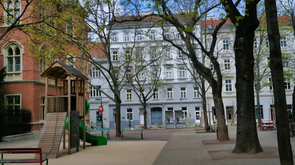 Ein urbaner Spielplatz in einer europäischen Stadt mit Bäumen und Wohngebäuden im Hintergrund.